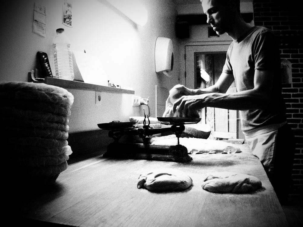 photo noir & blanc d'un boulanger en train de peser la pâte avec une vieille balance roberval à plateaux.